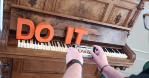 Orangefarbene Buchstaben-Deko, die "Do it" ergibt. Auf einem Klavier präsentiert