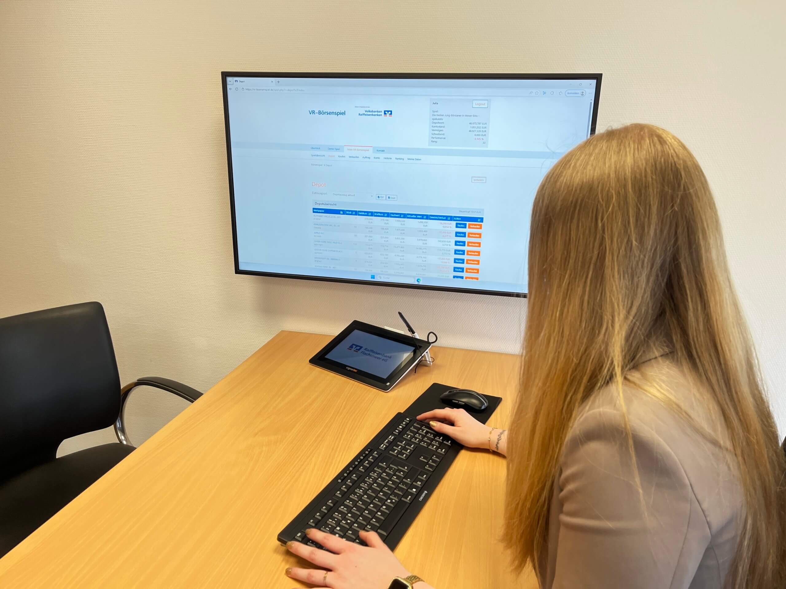Auszubildende vor Bildschirm mit Seite des VR-Börsenspiels